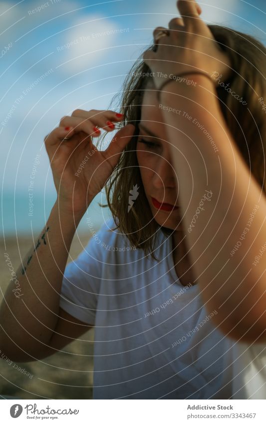 Junge Frau im Urlaub fixiert Haare am Meer berührend Behaarung Fixierung Strand Sand blau Himmel Einstellung rote Lippen Make-up lässig Zeitgenosse Hipster jung