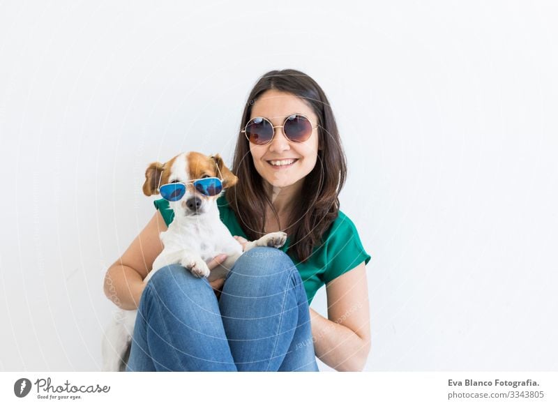 Hübsche junge Frau, die zu Hause mit ihrem kleinen süßen Hund spielt. Porträt des Lebensstils. Konzept der Liebe zu Tieren. weißer Hintergrund. Beide tragen eine Sonnenbrille