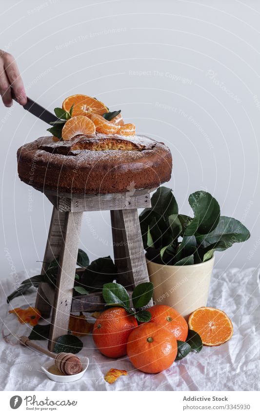 Person, die Zuckerpulver mit Teesieb über Kuchen gießt Mandarine Zitrusfrüchte Stillleben Frucht Hocker Dessert orange süß Gebäck Feinschmecker lecker hölzern