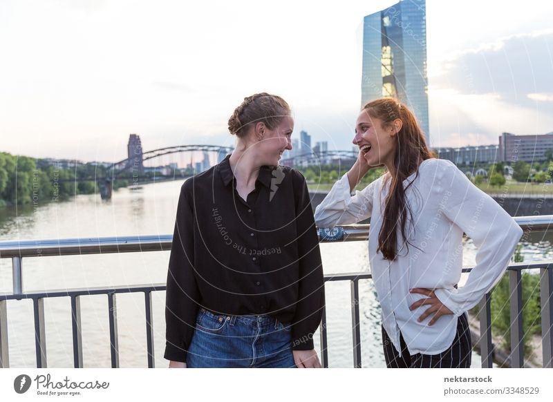 Zwei Frauen mit Blickkontakt auf der Brücke mit Stadthintergrund Erwachsene Freundschaft Jugendliche Skyline Lächeln Liebe Fröhlichkeit Mädchen reales Leben