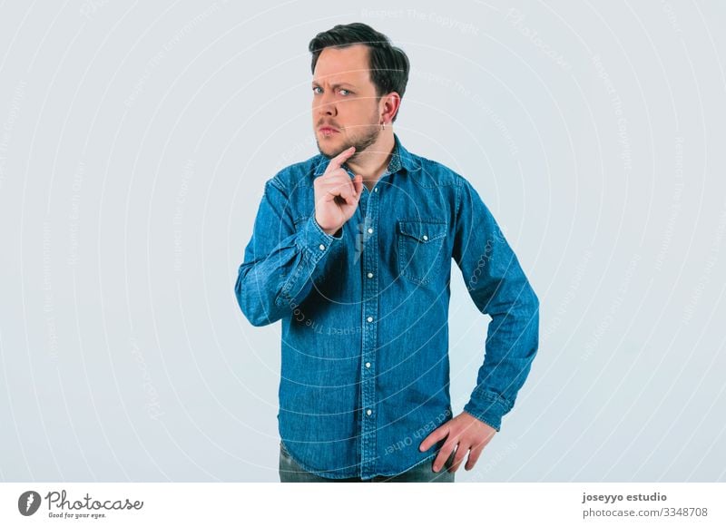 Junger Mann mit Ausdruck von Uneinigkeit und Entschlossenheit. Denim-Hemd und isolierter grauer Hintergrund. 30-40 Jahre Inserat Werbung analytisch Einstellung