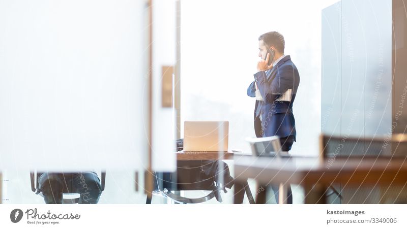 Ein Geschäftsmann, der mit dem Handy telefoniert und durch das Fenster schaut. elegant Schreibtisch Arbeit & Erwerbstätigkeit Beruf Arbeitsplatz Büro Business