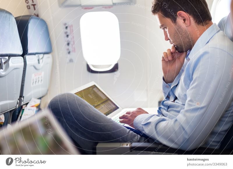 Lässig gekleideter Mann mittleren Alters, der während seiner Geschäftsreise in der Flugzeugkabine am Laptop arbeitet. Flache Tiefenschärfe Foto mit Fokus auf Geschäftsmann Auge.