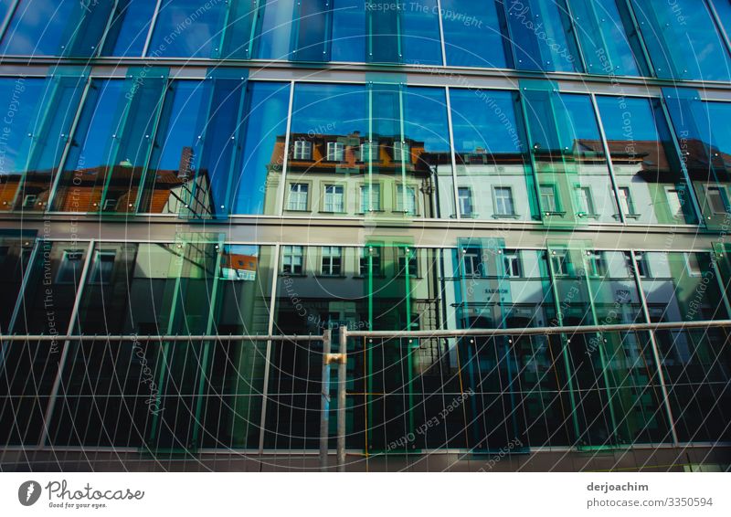 Häuserzeile mit verschiedenen Farben und einem blauen Himmel ,davor eine Glaswand. Reflexion & Spiegelung Wolken Sonne Licht Außenaufnahme sky reflection light