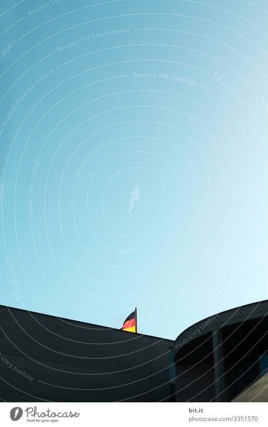 Fahne; Flagge von Deutschland an einem Mast, bei blauem Himmel im Regierungsviertel in Berlin, hinter einem Gebäude versteckt, im Sommer bei einem Ausflug während dem Urlaub in der Hauptstadt.