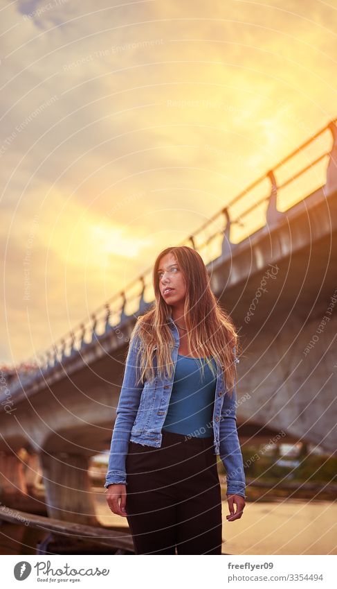 Porträt einer jungen Frau vor einer Stadtbrücke Lächeln Jeansstoff Jacke blau Sommer urban Brücke Zement blond Mädchen glühen Sonnenlicht Großstadt Gebäude Tag