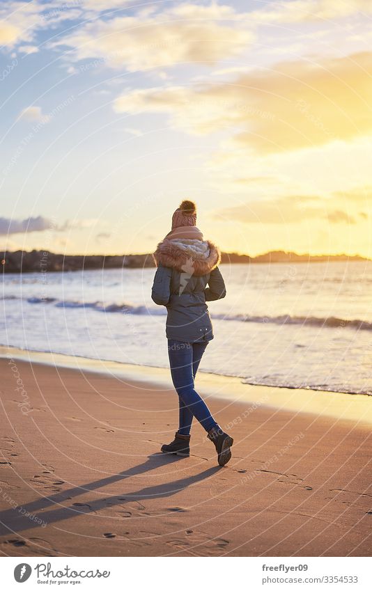 Junge Frau geht bei Sonnenuntergang in Vigo mit Winterkleidung am Strand spazieren jung rückwärts Bekleidung laufen Urlaub Menschen Sand MEER Herbst fallen