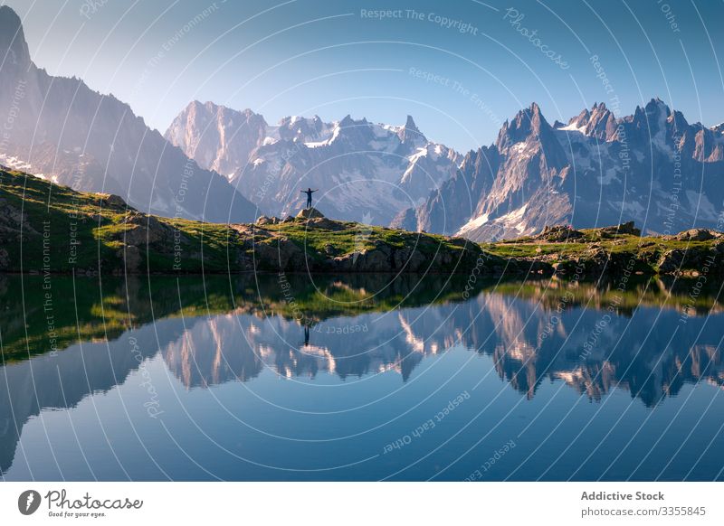 Einsamer Tourist an hügeligem Ufer, der sich im Kristallsee in schneebedeckten Bergen im Sonnenlicht spiegelt See Berge u. Gebirge Felsen verschneite