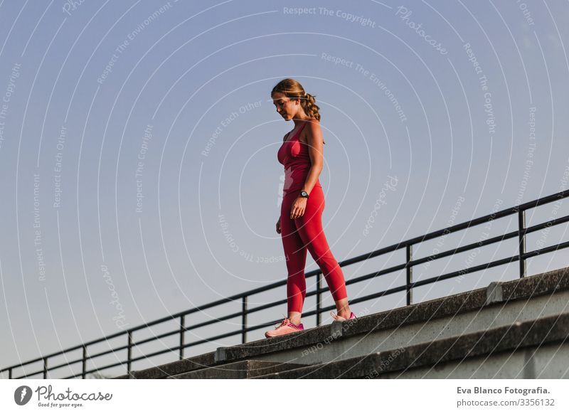 Fitness-Frau im Stadion, die bereit ist, Sport zu treiben. Tragen von roter Sportkleidung. Konzept für eine gesunde Lebensweise. Sonnenuntergang im Sommer