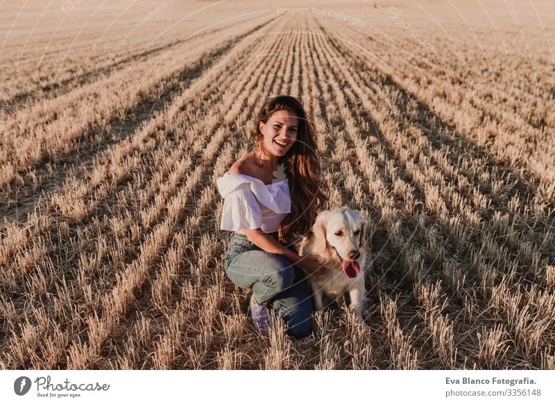 junge schöne Frau, die bei Sonnenuntergang mit ihrem Golden Retriever-Hund auf einem gelben Feld spazieren geht. Natur und Lebensstil im Freien Sommer Mode