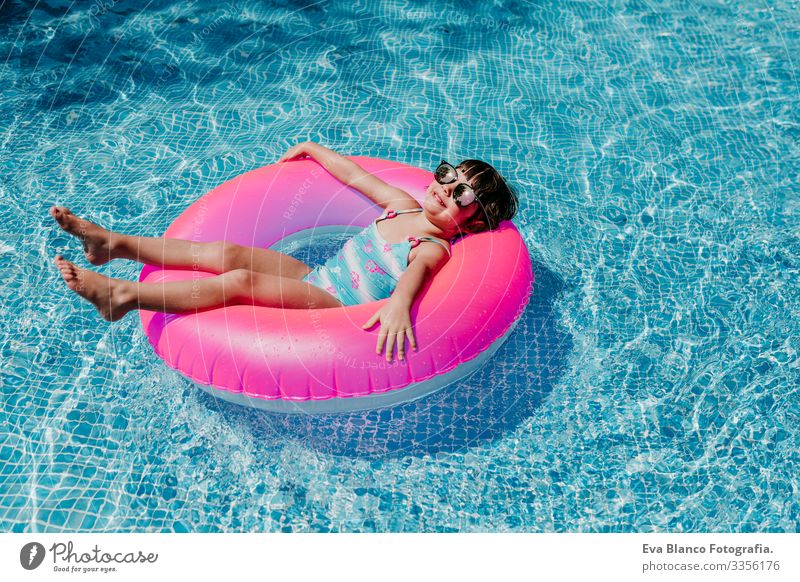 Hübsches Mädchen, das auf rosa Donuts in einem Pool schwimmt. Sonnenbrille tragen und lächeln. Spaß und sommerlicher Lebensstil Aktion Schwimmbad