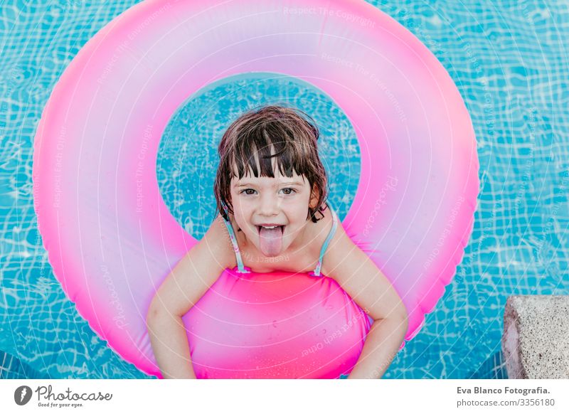 Hübsches Mädchen, das auf rosa Donuts in einem Pool schwimmt. Lächelnd. Spaß und sommerlicher Lebensstil Aktion Schwimmbad Beautyfotografie Außenaufnahme