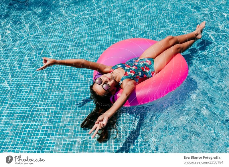 Ein wunderschöner Teenager schwimmt auf rosa Donuts in einem Pool. Sonnenbrille tragen und lächeln. Spaß und sommerlicher Lebensstil Aktion Schwimmbad