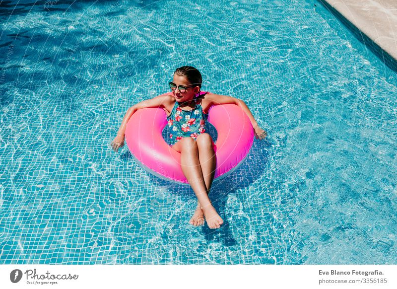 Ein wunderschöner Teenager schwimmt auf rosa Donuts in einem Pool. Sonnenbrille tragen und lächeln. Spaß und sommerlicher Lebensstil Aktion Schwimmbad