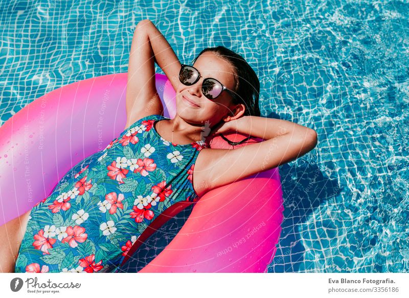 Ein wunderschöner Teenager schwimmt auf rosa Donuts in einem Pool. Sonnenbrille tragen und lächeln. Spaß und sommerlicher Lebensstil Aktion Schwimmbad