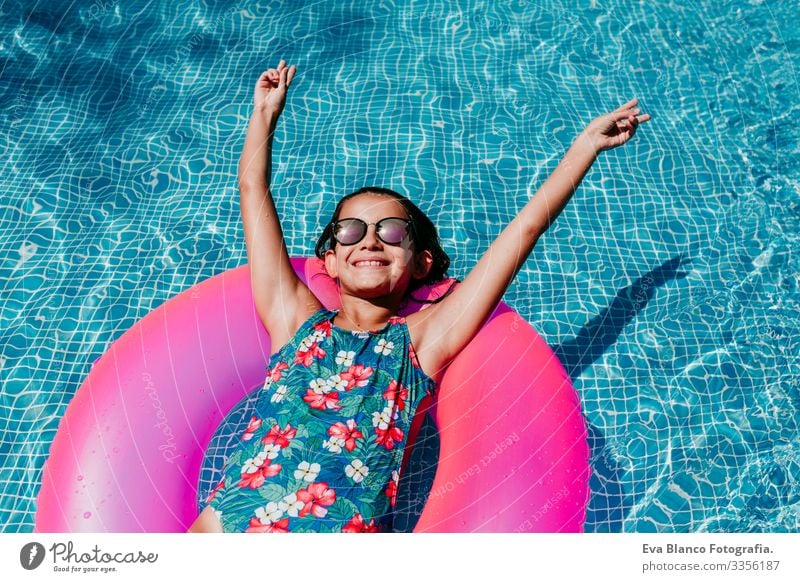 Ein wunderschöner Teenager schwimmt auf rosa Donuts in einem Pool. Sonnenbrille tragen und lächeln. Spaß und sommerlicher Lebensstil Aktion Schwimmbad