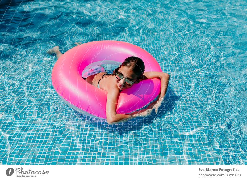 Ein wunderschöner Teenager schwimmt auf rosa Donuts in einem Pool. Sonnenbrille tragen und lächeln. Spaß und sommerlicher Lebensstil Aktion Schwimmbad