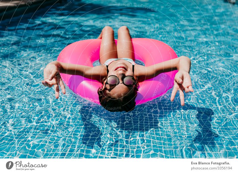 Ein wunderschöner Teenager schwimmt auf rosa Donuts in einem Pool. Sonnenbrille tragen und lächeln. Spaß und sommerlicher Lebensstil Aktion Schwimmbad