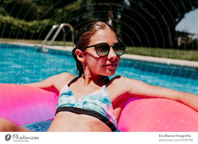 Ein wunderschöner Teenager schwimmt auf rosa Donuts in einem Pool. Sonnenbrille tragen und lächeln. Spaß und sommerlicher Lebensstil Aktion Schwimmbad