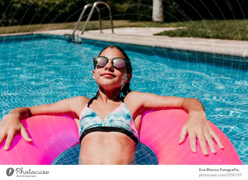 Ein wunderschöner Teenager schwimmt auf rosa Donuts in einem Pool. Sonnenbrille tragen und lächeln. Spaß und sommerlicher Lebensstil Aktion Schwimmbad