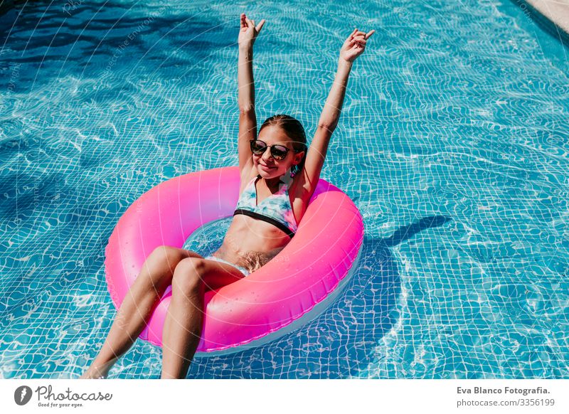 Ein wunderschöner Teenager schwimmt auf rosa Donuts in einem Pool. Sonnenbrille tragen und lächeln. Spaß und sommerlicher Lebensstil Aktion Schwimmbad