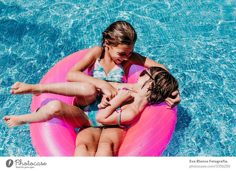 zwei wunderschöne Schwestern, die auf rosa Donuts in einem Pool schwimmen. Kitzeln und Lächeln spielen. Spaß und sommerlicher Lebensstil Aktion Schwimmbad