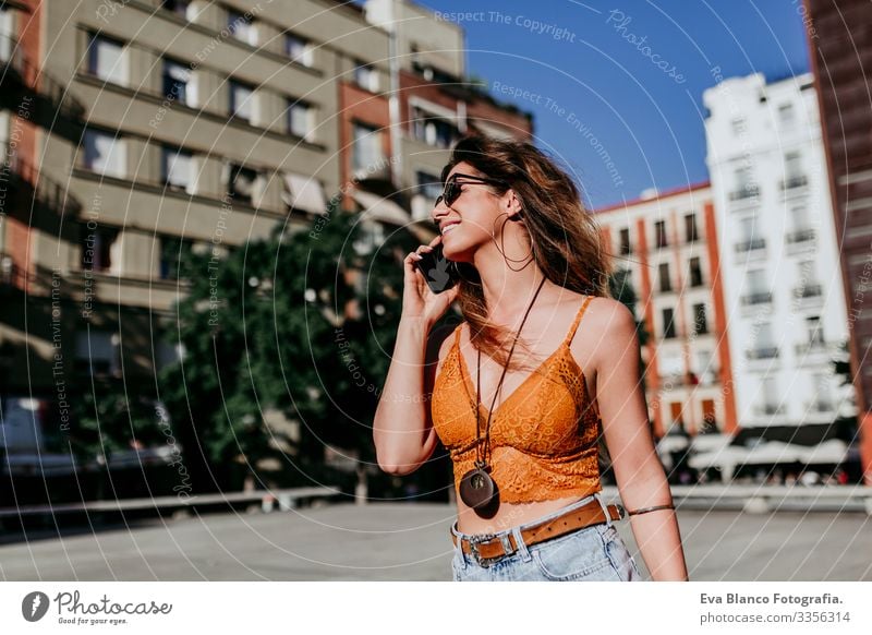 Hübsche junge kaukasische Frau, die an einem sonnigen Tag auf der Straße der Stadt spazieren geht. Sprechen mit dem Mobiltelefon. Glückliches Gesicht lächelt. Urbaner Lebensstil