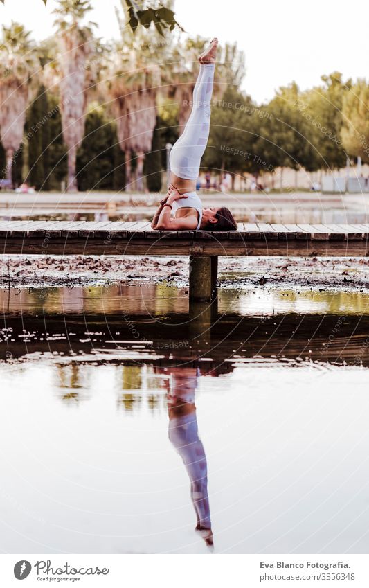 junge schöne asiatische Frau, die in einem Park Yoga macht. Auf der Brücke sitzend mit einer Reflexion auf dem Wassersee. Konzept für Yoga und gesunde Lebensweise