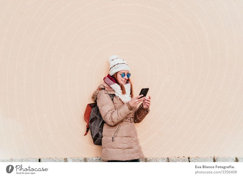 Frau, die ein Mobiltelefon über einem gelben Mauerhintergrund benutzt. Technik und Winterkonzept Außenaufnahme Großstadt Wand Handy Technik & Technologie