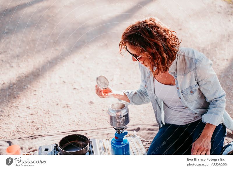 junge Frau, die im Freien mit Kanne und Herd Tee zubereitet. Camping-Konzept Jugendliche Topf Herd & Backofen Sonnenuntergang vorbereitend heiß Teekanne Kaffee