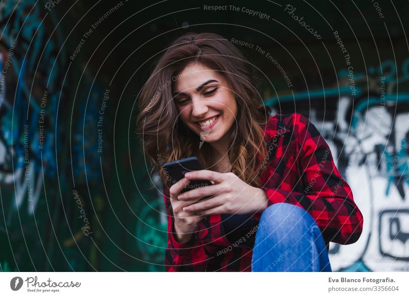 junge schöne Frau, die ein Mobiltelefon benutzt. Städtischer Graffiti-Hintergrund. Lebensstil im Freien.technologie Stadt Hut stehen attraktiv Mobile Zaun