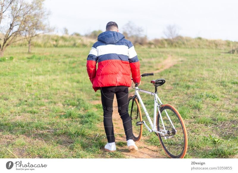 Rückansicht eines jungen Mannes, der mit einem feststehenden Fahrrad auf einem Park läuft Lifestyle Stil Glück Freizeit & Hobby Musik Telefon Handy PDA