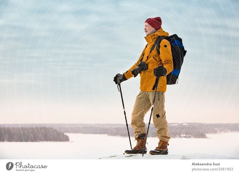 Porträt eines reifen Mannes mit grauem Bart, der Finnland im Winter erkundet. Reisender mit Kamera auf der Spitze des Felsens. Schöne Aussicht auf die nördliche Landschaft mit gefrorener Ostsee und verschneiten Inseln.