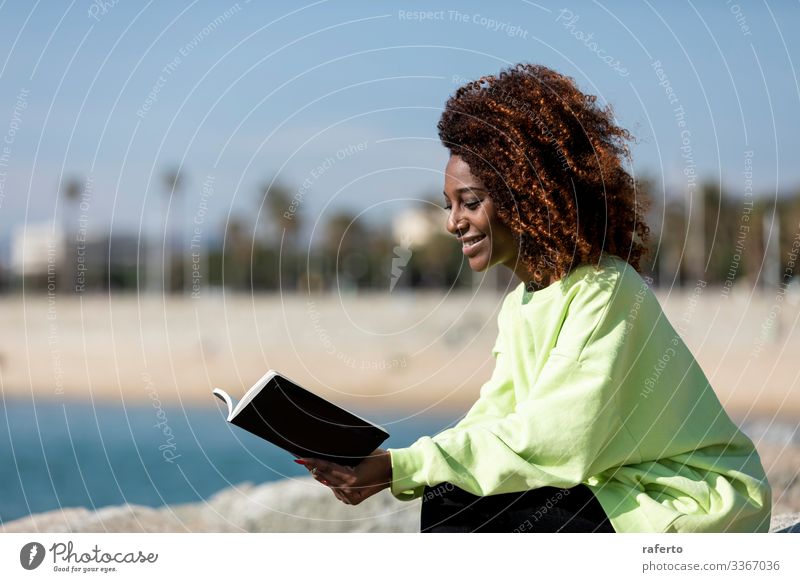 Seitenansicht einer Afro-Frau, die am Ufer sitzt und ein Buch liest Lifestyle Stil schön lesen Meer Mensch feminin Junge Frau Jugendliche Erwachsene 1