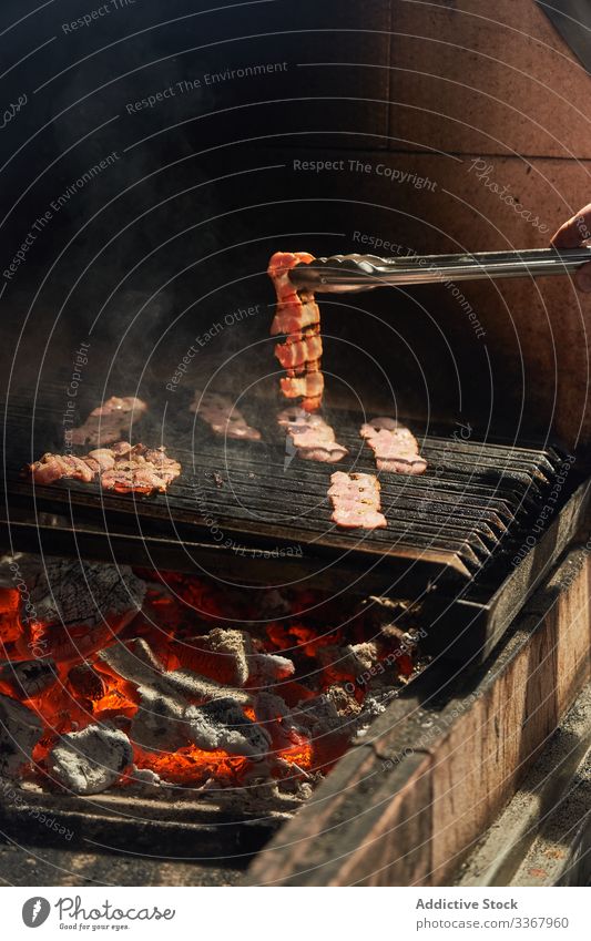 Gesichtsloser Mann wendet Speckscheiben auf Grillrost Küchenchef Barbecue Flip drehen. Zange Koch Garten gebraten Fleisch Ablage Lebensmittel Vorbereitung