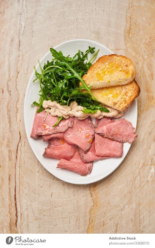 Leckeres Fleisch mit Brot und Rucola Speise Teller Schinken Jamón Restaurant frisch grün Kraut Tisch hölzern Salatbeilage Scheibe stylisch elegant Haute Cuisine