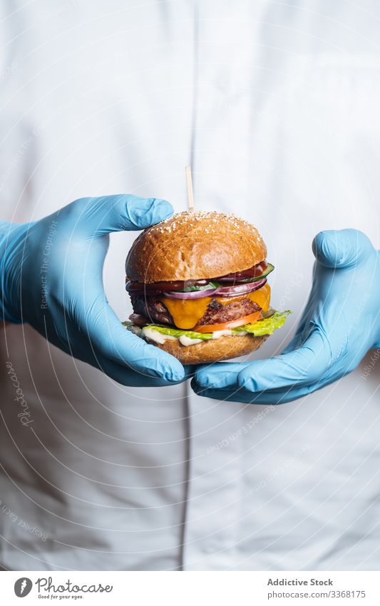 Anonyme Person mit Burger mit gebratener Frikadelle und frischem Gemüse Fastfood Straßenessen Speise Restaurant Pastetchen Saucen Zwiebel Salat Hirschfleisch