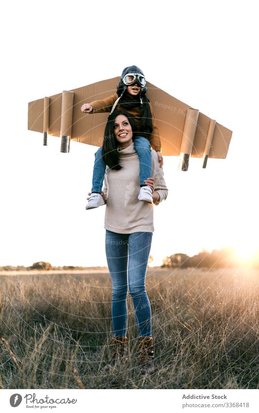 Fröhliche Mutter und Sohn spielen zusammen auf dem Feld Frau Mama Flieger träumen Spiel Zusammensein Junge anhaben Schutzbrille Flügel imitieren Wiese Karton