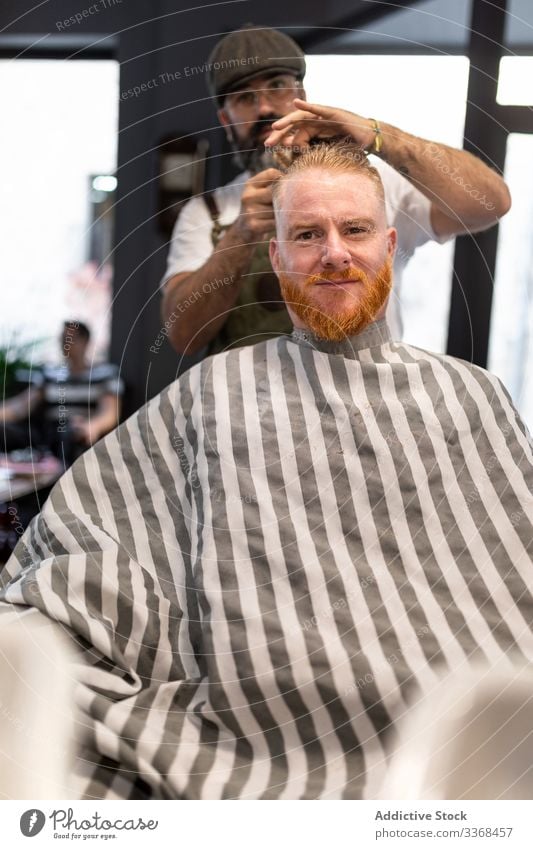 Friseur schneidet einem rothaarigen Mann die Haare Klient trendy Barbershop bärtig Maskulinität Kunde Behaarung Pflege Salon Hipster gutaussehend stylisch