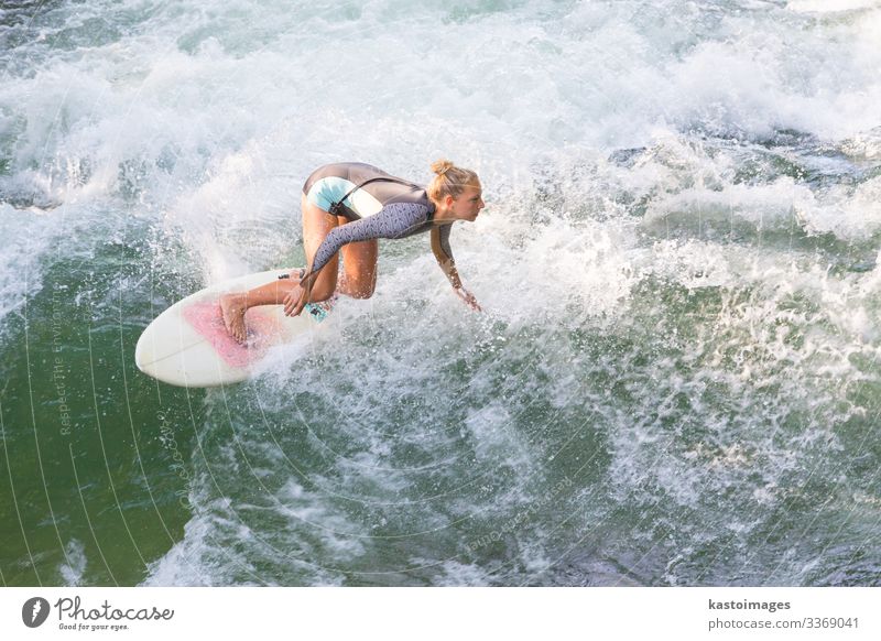 Attraktives sportliches Mädchen in Neopren-Shorty beim Surfen auf der berühmten künstlichen Flusswelle im Englischen Garten, München, Deutschland. Lifestyle