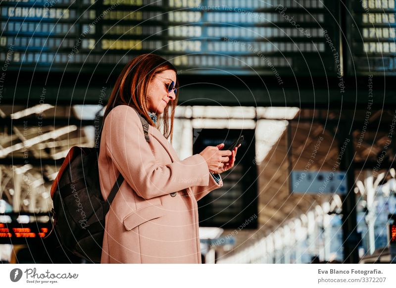 junge Frau am Bahnhof, die auf die Zieltafel schaut. Konzept für Reisen und öffentliche Verkehrsmittel Bildschirm Ausflugsziel reisen Rucksack Rückansicht