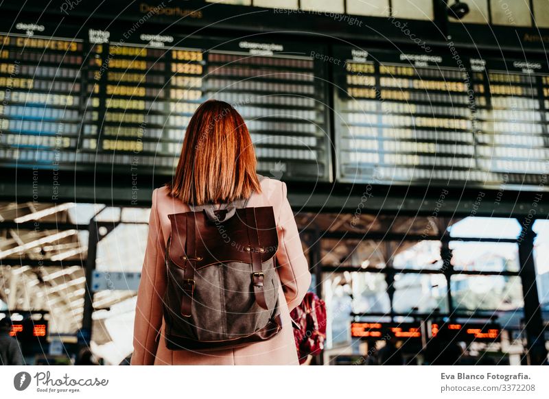 junge Frau am Bahnhof, die auf die Zieltafel schaut. Konzept für Reisen und öffentliche Verkehrsmittel Bildschirm Ausflugsziel reisen Rucksack Rückansicht