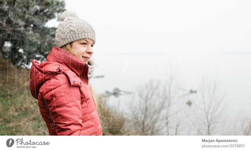 Junge Frau steht am Wintermorgen am Fluss aktiv Erwachsener Abenteuer allein schön Verschlussdeckel lässig Kaukasier Küste kalt genießend frei Freiheit Frost