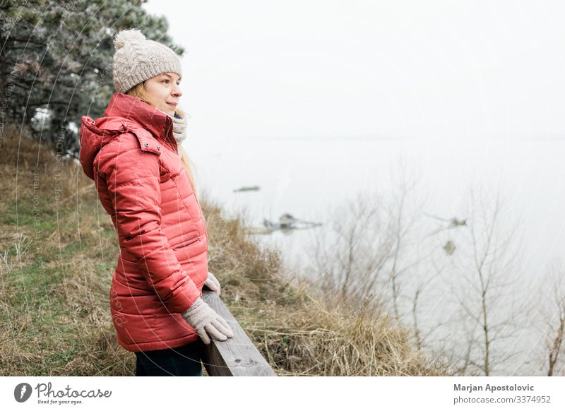 Junge Frau steht am Wintermorgen am Fluss aktiv Erwachsener Abenteuer allein schön Verschlussdeckel lässig Kaukasier Küste kalt genießend frei Freiheit Frost