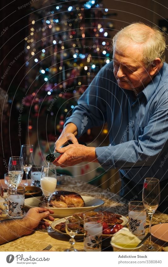 Alter Mann schenkt beim Weihnachtsessen zu Hause Champagner in Gläser ein Weihnachten feiern heimwärts Flasche Glas gealtert Senior lässig trinken Getränk