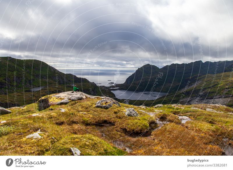 Eine Person sitzt auf einem Felsen und genießt den Blick von den Bergen auf den Lofoten auf das Meer bei einer Wanderung. Lofoten Inseln Norwegen Norwegenurlaub