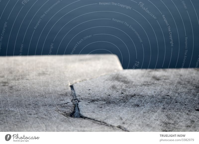 Blick auf zwei helle zusammengefügte Steinblöcke einer Mauer mit einem See dahinter Vogelperspektive Schwache Tiefenschärfe Kontrast Gedeckte Farben grau