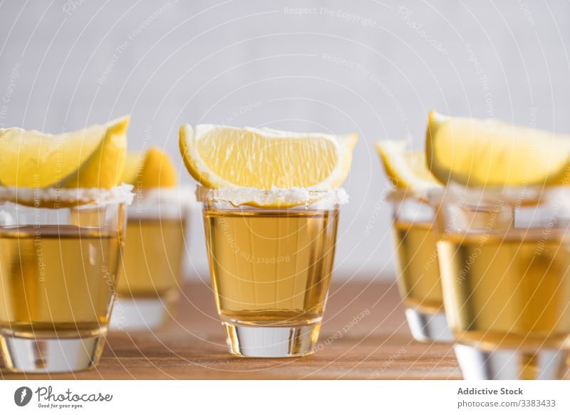 Schuss Alkohol mit Zitronenscheiben oben drauf Tequila Scheibe Spielfigur Schnaps Reihe Glas Tisch hölzern Wand trinken Getränk Erfrischung geschmackvoll kalt