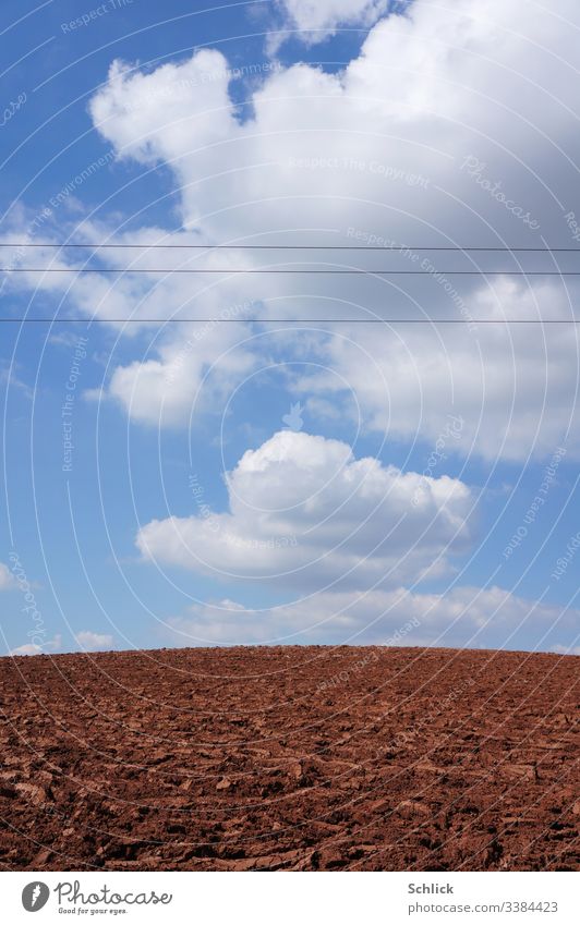 Kahler Acker und Himmel mit Kumulus Wolken von Hochspannungsleitungen durchschnitten Monokultur Feld Stromleitung Horizont Hügel Kulturlandschaft Ackerbau