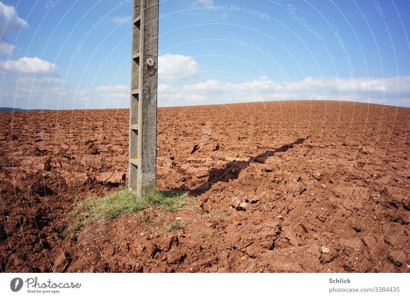 Acker mit nackter Erde und Strommast mit Schild Lebensgefahr unter blauem Himmel Monokultur Text Pestizide Gefahr Landwirtschaft Hinweis doppeldeutig braun weiß